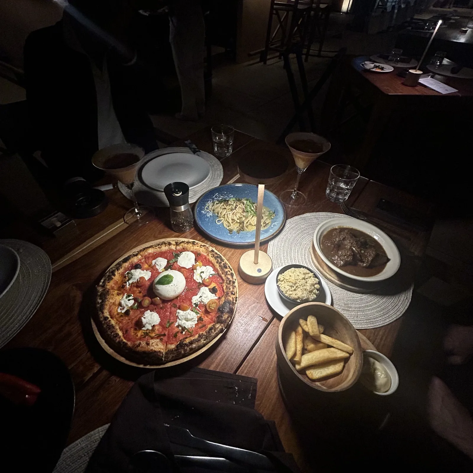 A burrata pizza with fries and cocktails on a wooden table at Carpe Diem, Phuket